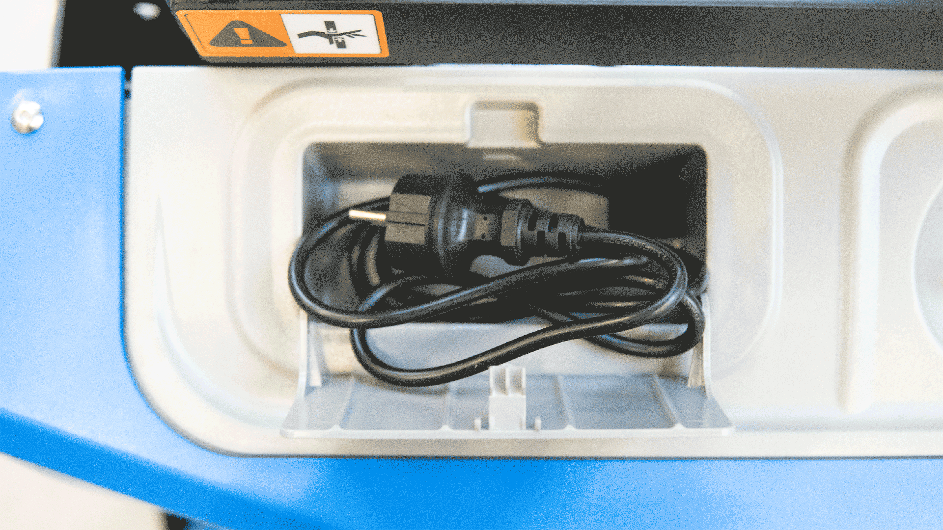 Ladefach mit aufgewickeltem Netzkabel und Netzstecker auf blauer Geräteverkleidung in Detailansicht